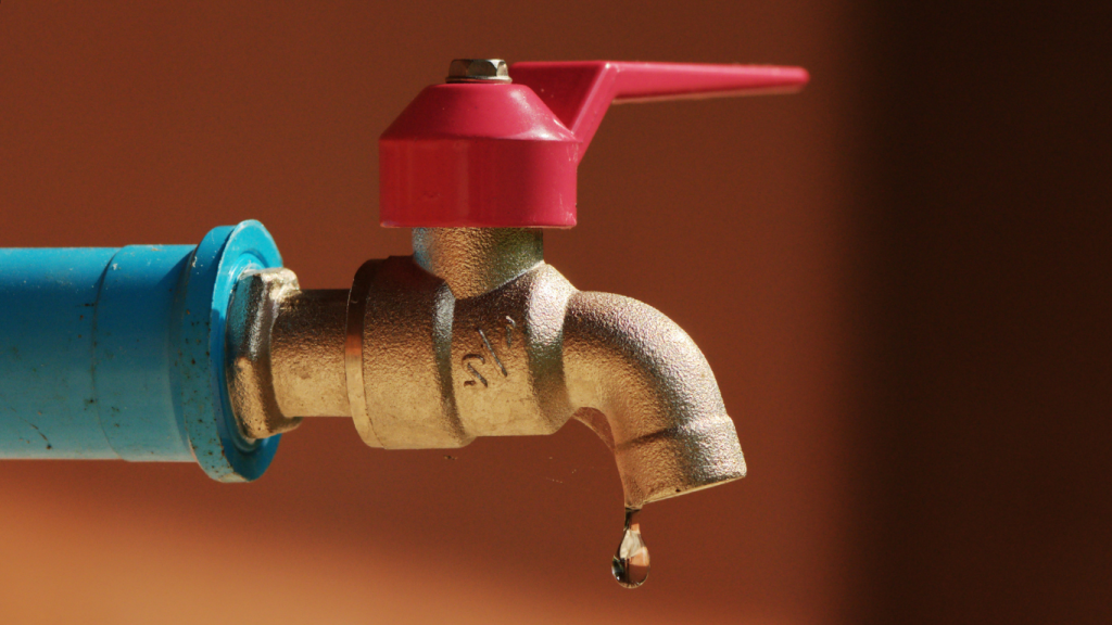A picture of a metallic tap with a blue pipe and red knob for opening and closing. The picture is being used by Ambokili Farm to symbolise the need for water conservation especially in semi-arid regions.