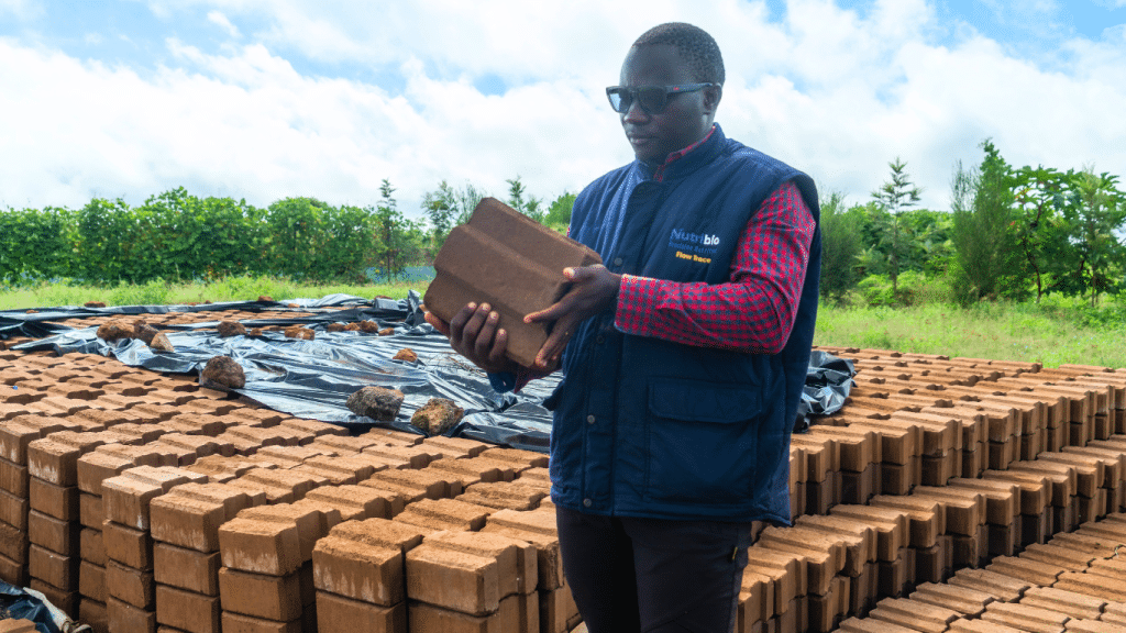 An employee at Ambokili Farm holding an interlocking block. The picture demonstrates Ambokili Farm's passive housing or bioclimatic architecture project.